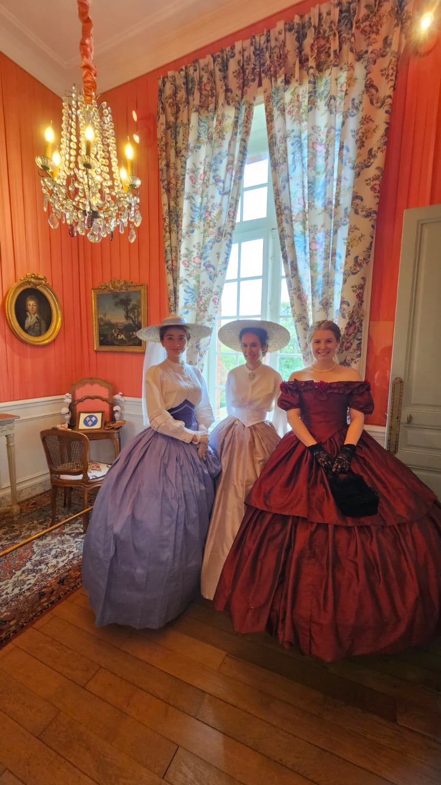 Trois participantes en robes à crinoline dans un salon du Château de Breteuil